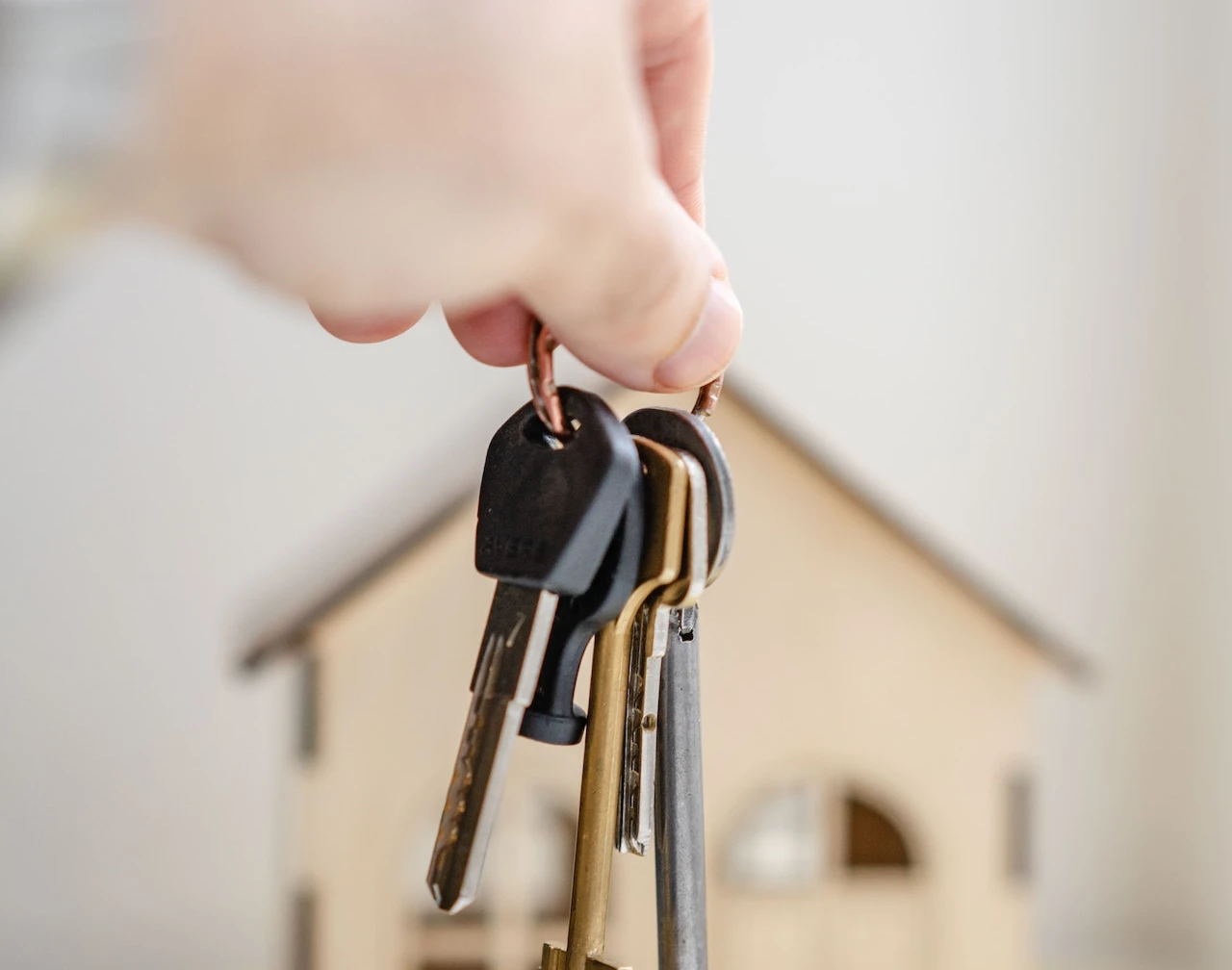 a hand holding some house keys with a house in blurred in the background