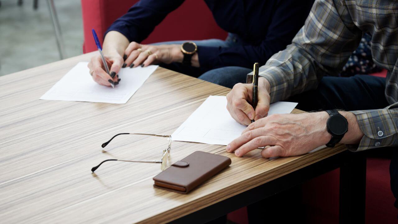 An adult woman and a man, sitting at a table in the office, fill out documents or forms. The concept of a marriage contract, agreement or divorce proceedings